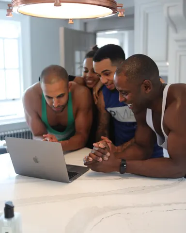 Peter Mac, Rochelle Humes, Aston Merrygold and Marvin Humes gathered round a laptop at a kitchen worktop